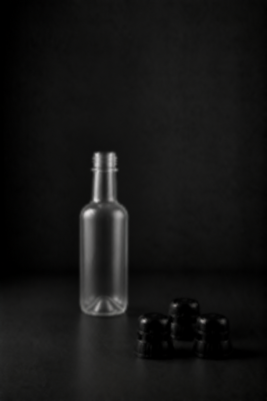 Bewusst unscharfe Vorschau einer kleinen offenen PET-Flasche ohne Etikett mit drei InCap-Kappen